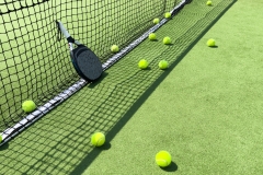 Padel racket and padel ball on a green court in the sunset