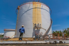 The male worker takes the cable car holding an industrial painting white color brush used for shell plate tank oil surface