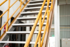 Banister handrail with yellow painting of stairway platform at the factory place. Industrial building structure part photo, Close-up and selective focus at handrail.