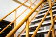 Banister handrail with yellow painting of stairway platform at the factory place. Industrial building structure part photo, Close-up and selective focus at handrail.