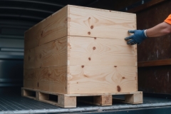Person in orange vest is loading large wooden crate onto pallet inside delivery truck. scene conveys sense of logistics and transportation