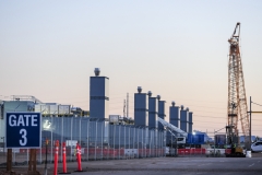 Data center construction site with fenced perimeter, crane, exhaust stacks, and equipment, showing active development of secure technology infrastructure for computing, storage, and network operations