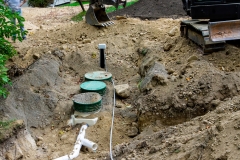 Partially buried treatment tank and UV disinfector with pipe connected, and the drain field in the background at a home septic system installation