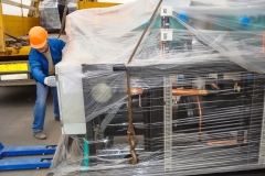 A worker is carefully unloading a large industrial chiller from a truck using a pallet jack.