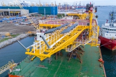 yellow offshore oil and gas platform structure being loaded onto a heavy transport vessel at an industrial port shipyard for construction, representing maritime logistics, offshore energy, and heavy engineering.