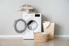 Modern washing machine with laundry near white wall