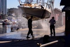 2 people pressure washing hanging boat in marina