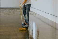 Worker, coating floor with self-leveling epoxy resin in industrial workshop.