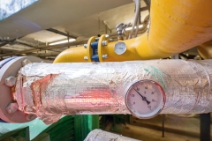 Industrial thermometer on insulate system pipe in silver foil.