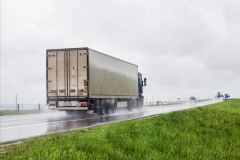 A trucker on a truck with a semitrailer transports cargo in poor visibility on the road, rain. Highway traffic in bad weather. Copy space for text
