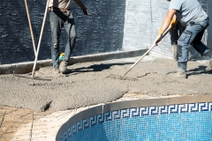 Workers distributing the concrete with rakes around the pool, fixing the garden