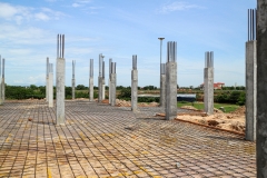 A construction site with concrete columns and reinforcing steel bars, showing the framework for a new building project. Concrete pillars and a steel mesh floor await the next stage of construction.