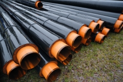 Steel pipe with heat insulation lay on the ground. Water main replacement equipment, stack of insulated pipes for pipeline, underground heat system.