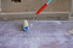 Priming the concrete floor with a roller. Professional floor primer. Leveling concrete floors. Floor repair using a primer.