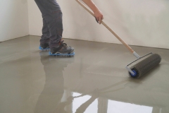 A worker rolls out the liquid floor with a trowel. Squeegee for distributing the mixture. The worker levels the liquid floor. Finishing works - Needle roller for bulk floor