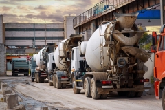 Heavy mixer concrete trucks waiting for to be loaded on the concrete mixing and batching factory. Deficiency of concrete and sand formed a queue for loading at the building materials factory.