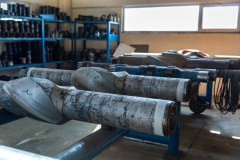 Different types of drill bits used in the oil exploration industry and spare parts in the background, ready to use in the closed warehouse area